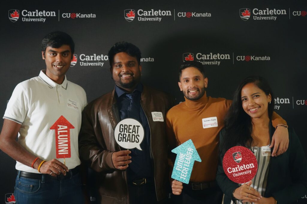 Four people posing with alumni photobooth props