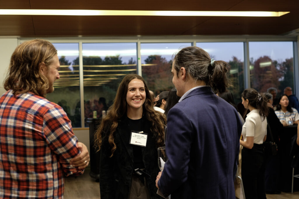 Three people smiling engaged in conversation at the economics alumni reception