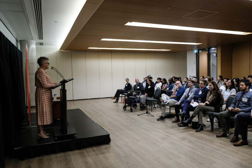 Brenda O'Neill speaking at podium in front of crowd of attendees of the economics alumni reception