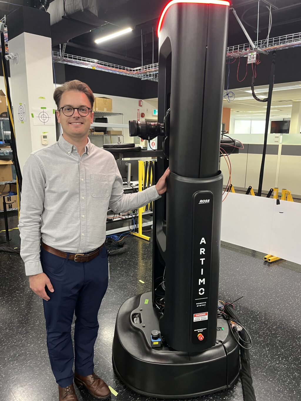 Nick Simpson stands beside Artimo, the award-winning studio robot, in Ross Video's robotics studio.