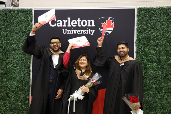 Three graduating students cheer and hold their diplomas up in the air