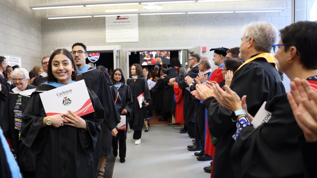Graduate proudly holds their diploma up as they exit the fieldhouse after convocation