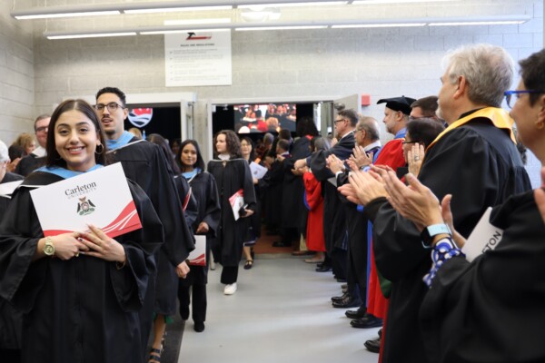 Graduate proudly holds their diploma up as they exit the fieldhouse after convocation