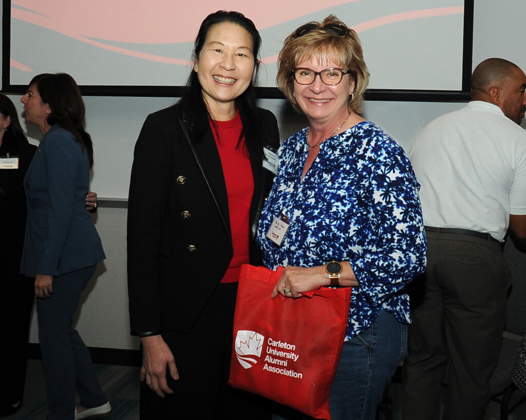 a photo of two women smiling, one holding a red Carleton bag. 