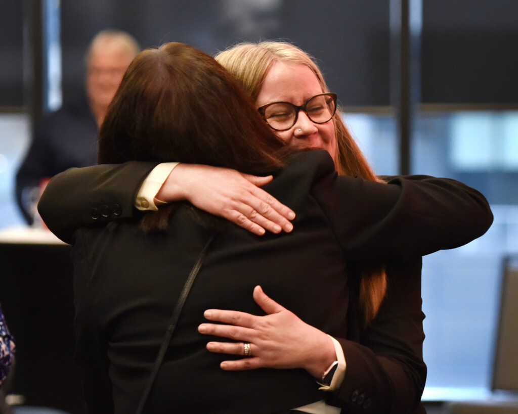 a photo of a woman wearing black glasses, hugging another person. 