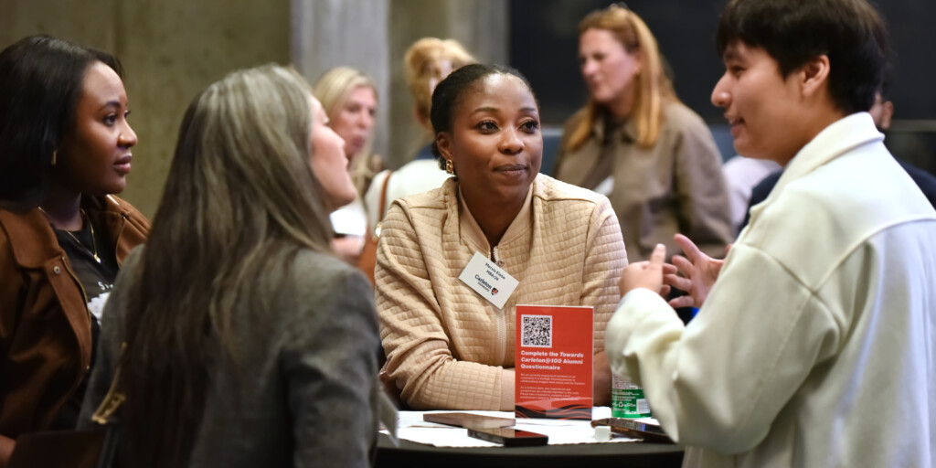 a photo of a person leaned over a high-top table, wearing a brown sweater and a name tag.