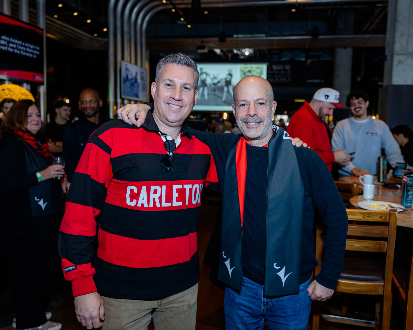 Two people wearing Carleton and Ravens gear smile for a photo