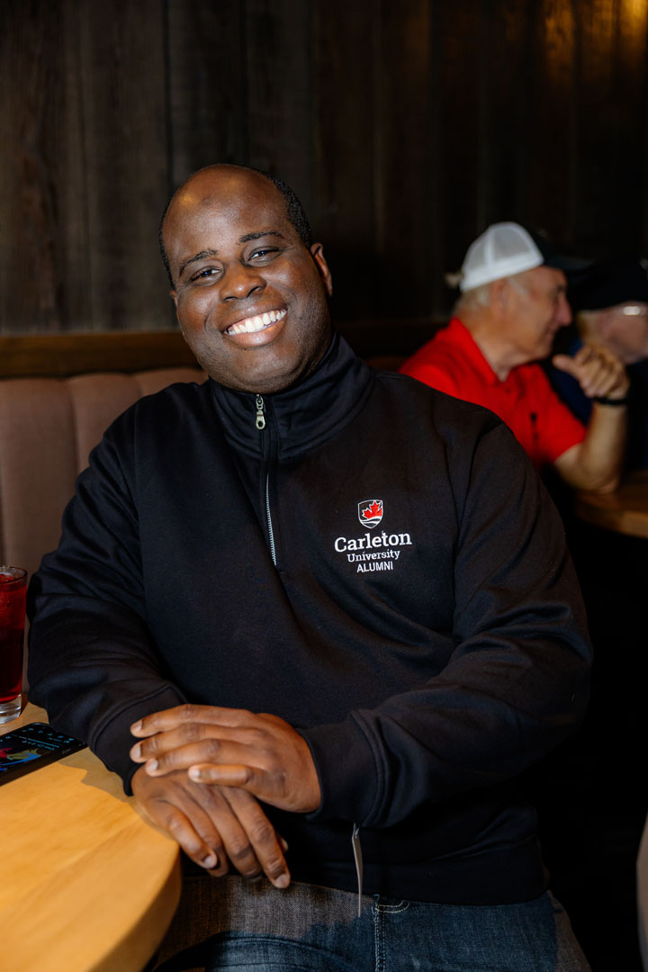 Person smiles wearing a Carleton University Alumni quarter zip sweater