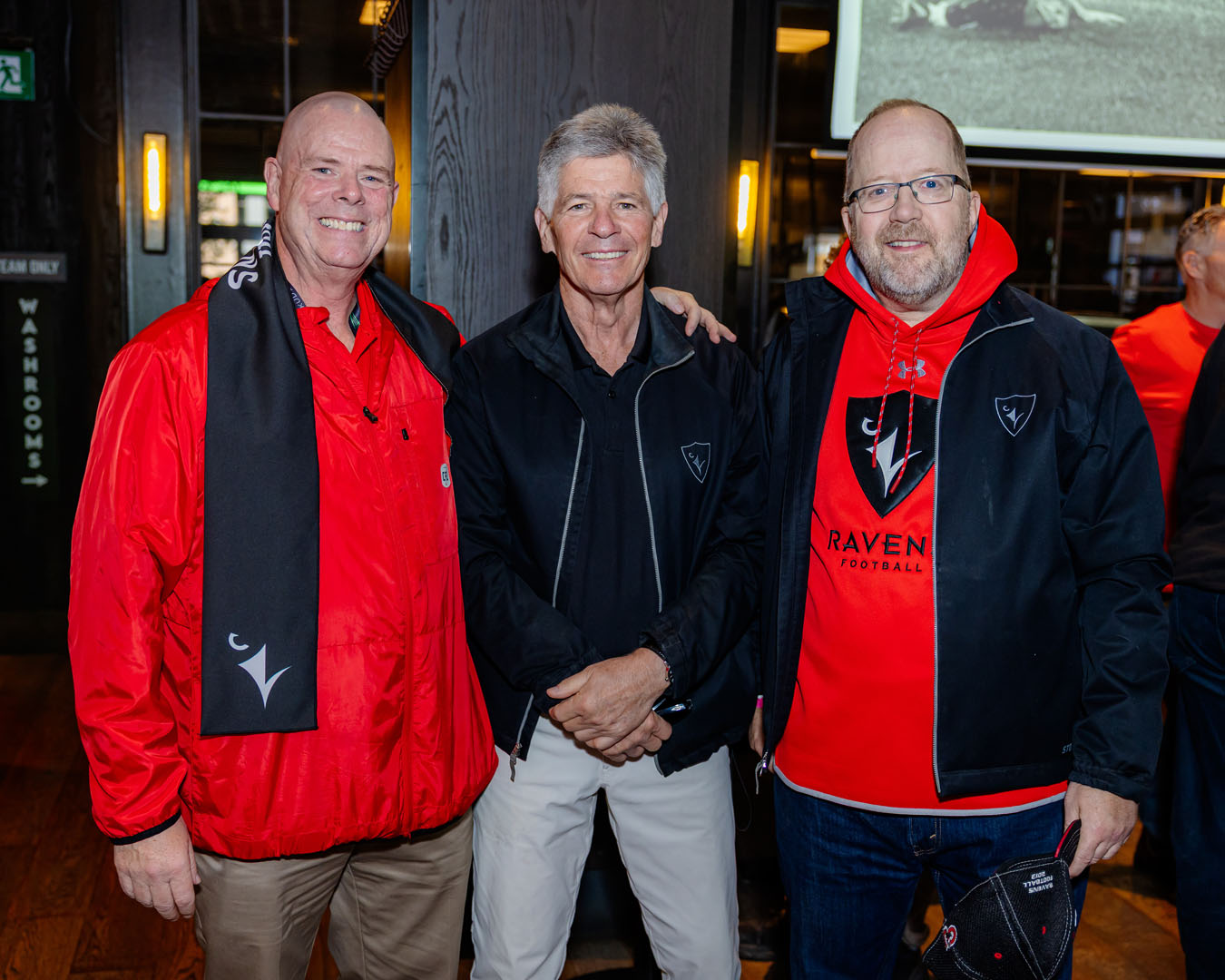 Three people in Ravens gear smile for a photo
