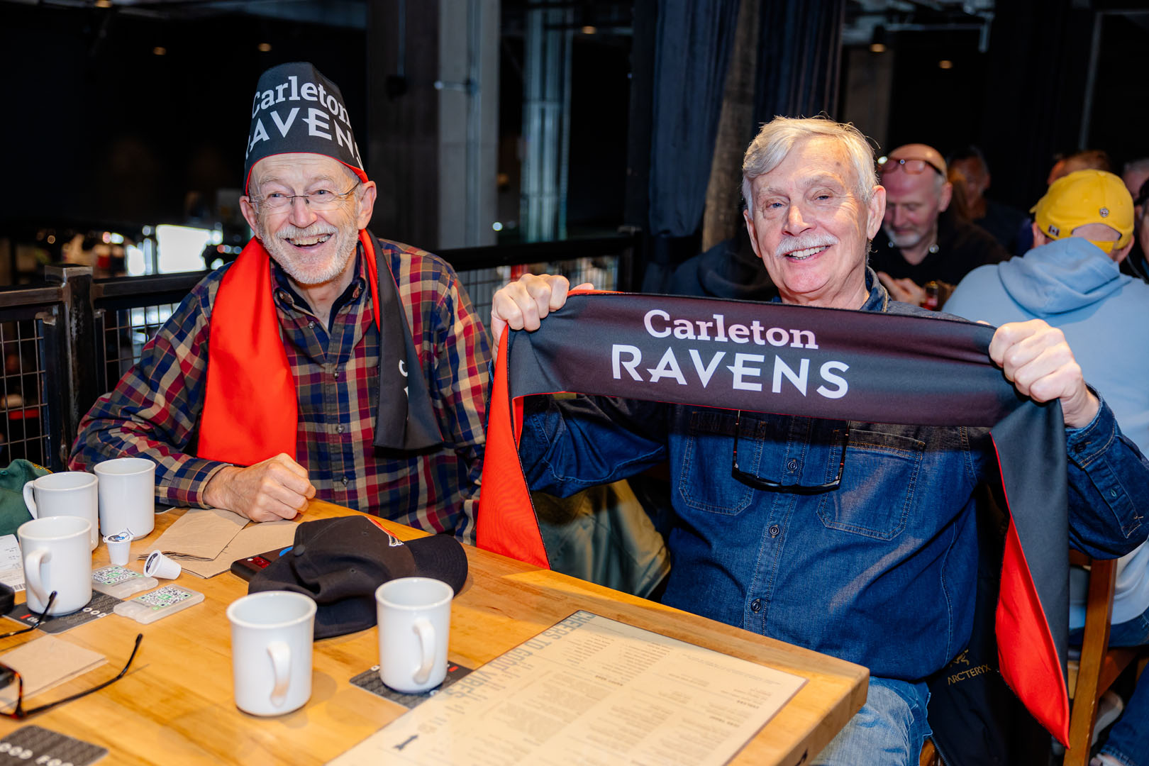 Two people pose for a photo with their Carleton Ravens scarves