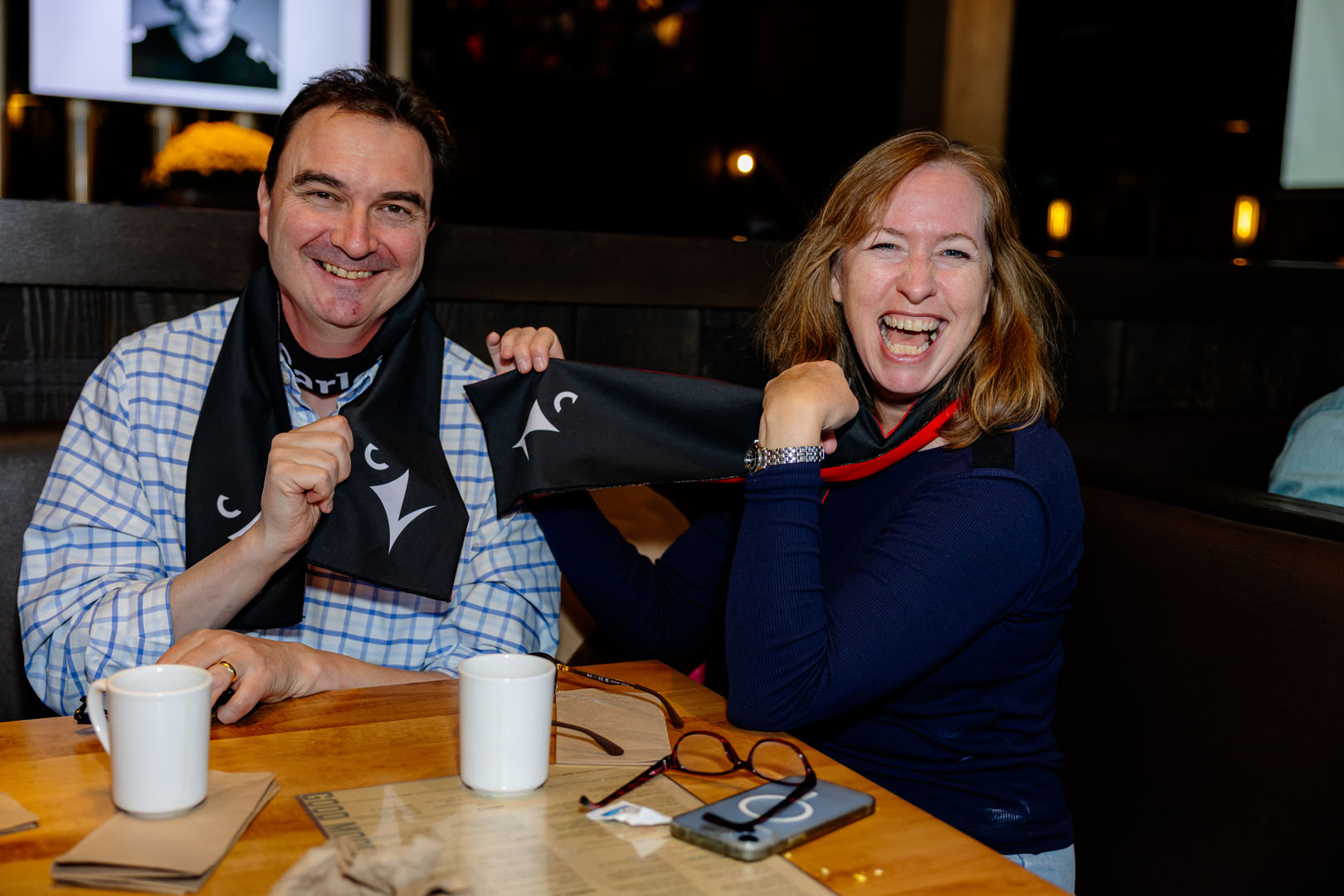 Two people smile showing their Ravens scarf at the Pancaker Breakfast