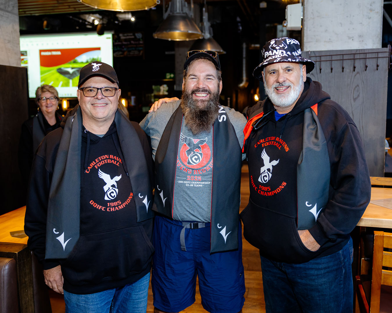 Three people smile, all wearing Ravens scarves, at the Pancaker Breakfast
