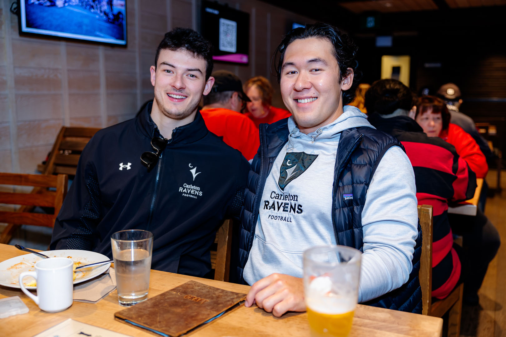 Two guests, wearing Ravens Football sweaters, smile at the Pancaker Breakfast