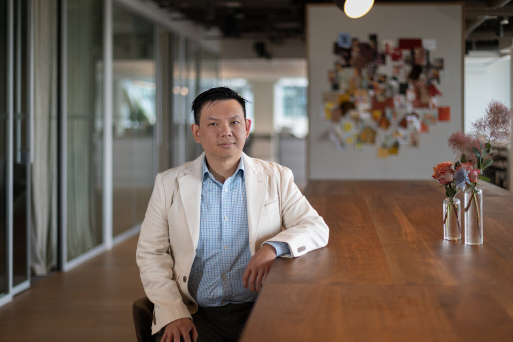 A photo of Tommy Ong sitting at a wooden table with his elbow resting on the table.