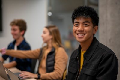 Student smiling in the foreground, with two other students in the background